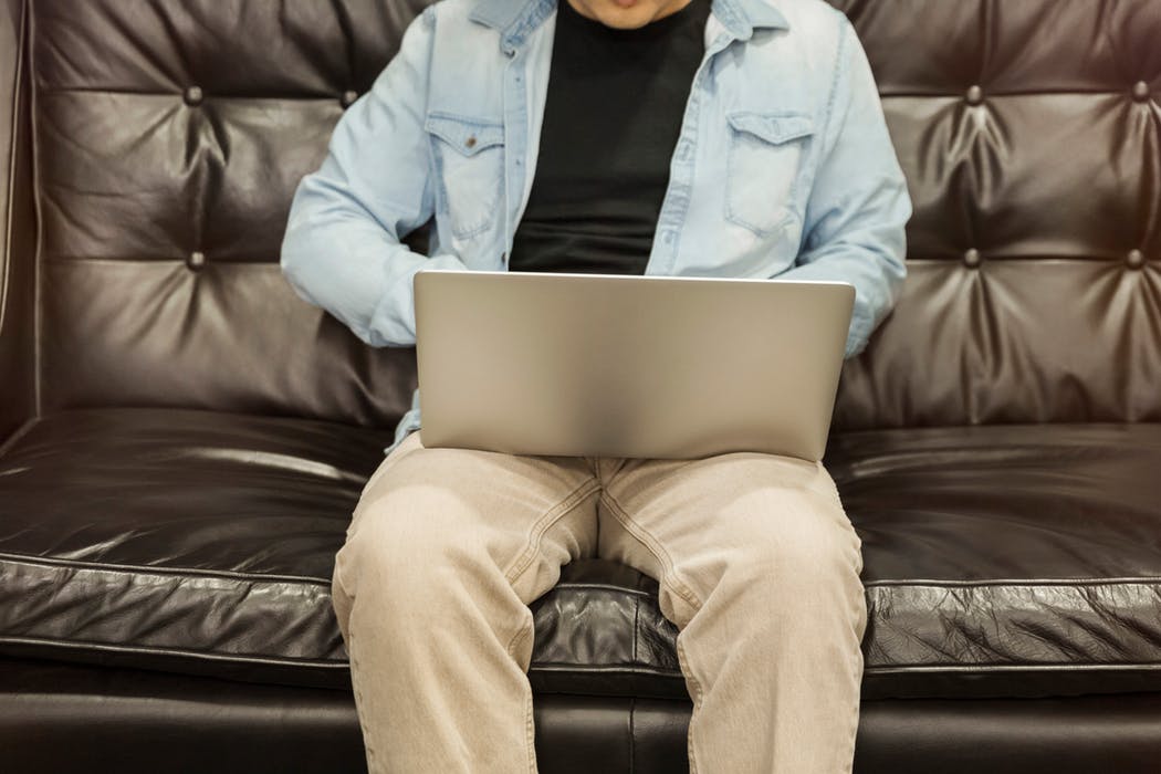 man sitting in a leather sofa while holding a laptop